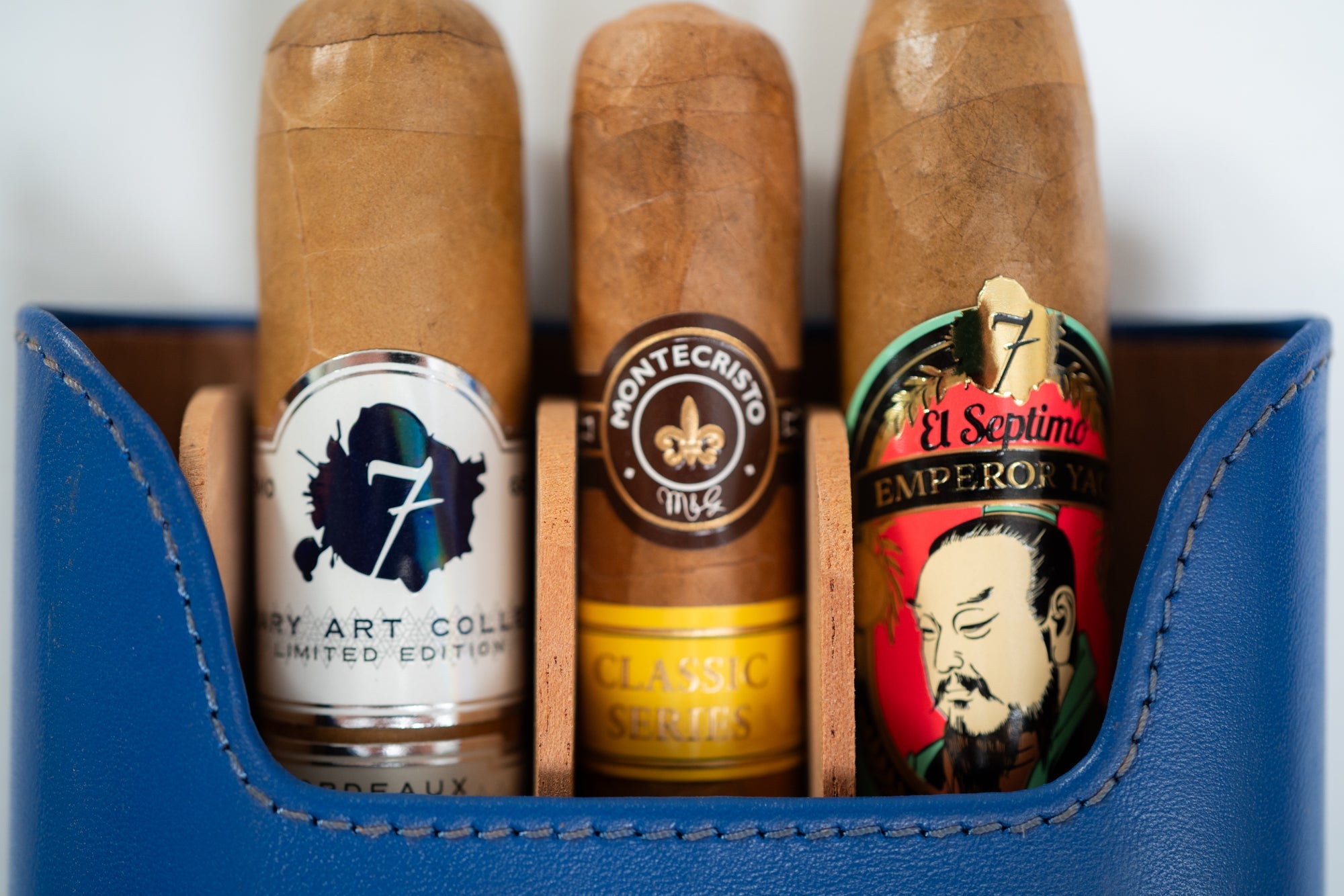 Three premium cigars in a blue leather case featuring El Septimo Emperor cigar, Montecristo cigar and an El Septimo limited edition cigar.